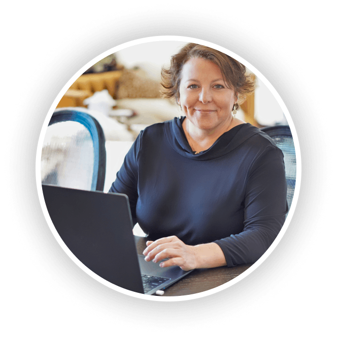 Suzanne smiling while working on a laptop at a desk in a bright, modern space.